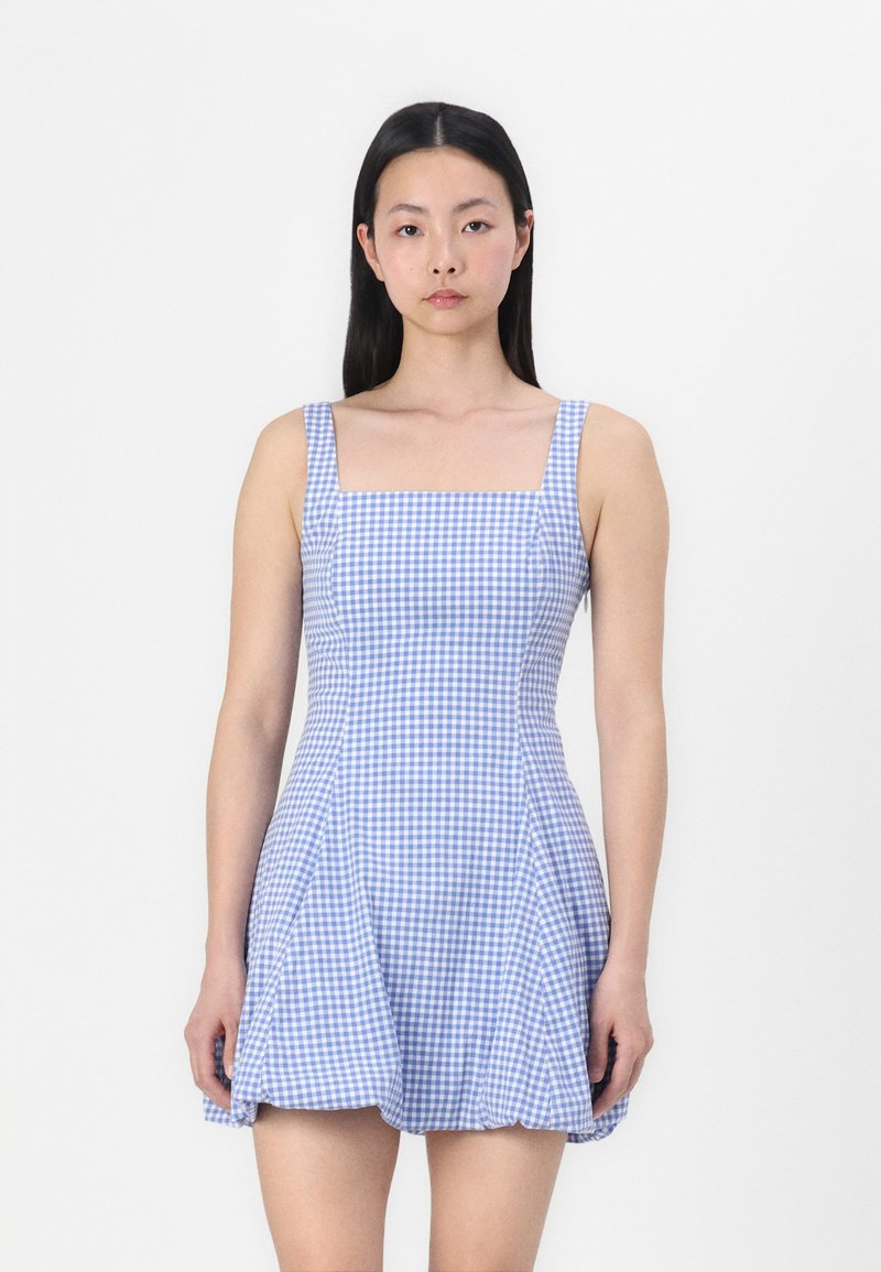 Robe à carreaux bleus et blancs avec un décolleté carré, des fines bretelles et une jupe évasée. Fabriquée en tissu léger, offrant une texture douce.