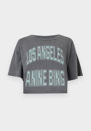 Personne portant un t-shirt gris oversized court avec le texte « LOS ANGELES ANINE BING », un jean bleu ample, une ceinture noire, des chaussures pointues et des lunettes de soleil noires.