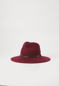Széles karimájú burgundi színű gyapjúkalap sötétbarna fonott bőrszíjjal és egy kis fém márkacímkével fehér háttér előtt.