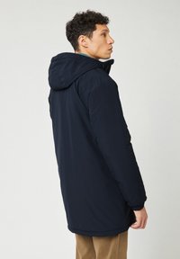 Parka aislante azul marino con capucha, con un acabado mate, puños elásticos y un respaldo ligeramente más largo para mayor cobertura.