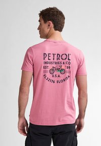 Růžové bavlněné tričko s černým potiskem "PETROL INDUSTRIES & CO" a grafikou motocyklu na zadní straně, krátké rukávy, kulatý výstřih.