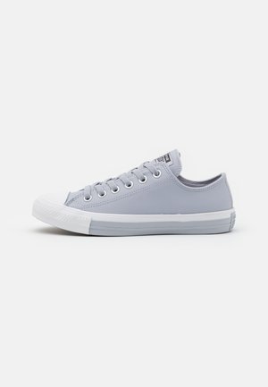 Jasnoszary niski sneaker z białym gumowym noskiem, białą podeszwą, metalowymi oczkami i sznurowadłami na jednolitym białym tle.