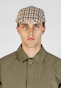 Cappello a scacchi in marrone chiaro, marrone e blu navy; design piatto. Il modello indossa un giubbotto verde oliva con colletto abbottonato. Sfondo bianco.