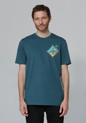 Teal cotton t-shirt featuring a diamond-shaped graphic with palm trees and a beach scene on the left chest. Short sleeves, standard fit.