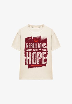 Cream-colored t-shirt featuring a graphic design in red with text "REBELLIONS ARE BUILT ON HOPE" on a textured background. Short sleeves.