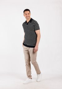 Polo de rayas en blanco y negro de manga corta, combinado con pantalones beige y zapatillas blancas. Tela suave con cuello de polo y detalle del logo en el lateral.
