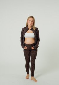 Legginsy i dopasowana kurtka o wzorze w cętki lamparta, wykonane z elastycznego materiału. Zestaw ma dopasowany krój, bez guzików, w brązowo-czarnej kolorystyce.