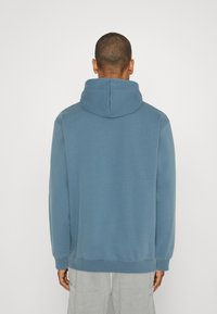 Felpa blu con cappuccio, caratterizzata da una texture liscia e polsini a coste. Il design è semplice, senza motivi visibili o dettagli hardware.