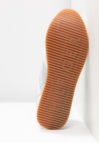 Gumová podrážka s texturovaným a žebrovaným vzorem; bílý svršek s šedými akcenty a síťovinou pro prodyšnost.