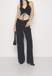 Black crop top with a V-neck and gathered detail, paired with high-waisted black wide-leg jeans. Accessories include a small black handbag.