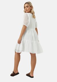 Vitt klänning med rutmönster, korta puffärmar och en flerlagrig kjol. Stylar med bruna sandaletter för kontrast.