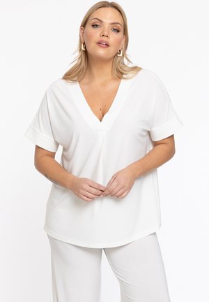 Witte korte mouwen top met een V-hals, zachte stof en opgerolde mouwen. Subtiele zijsplitten en een losse pasvorm. Gekocht met bijpassende lichtgekleurde broek.