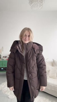 Hnědý prošívaný kabát s vysokým límcem, žebrovanými detaily a zipem. Má prošívanou texturu a polodlouhý střih.