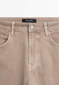 Beżowe dżinsy o prostym kroju, z metalowym zapięciem na guziki, paskami oraz kieszeniami z przodu. Metka z napisem "Massimo Dutti."