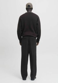 Czarny, fakturowany sweter z długimi rękawami, w połączeniu z luźnymi czarnymi spodniami. Model nosi czapkę w wzór.