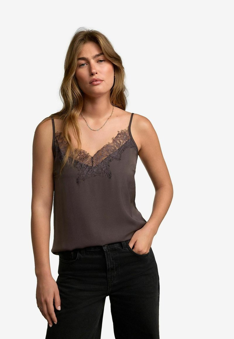 Camisole in satin grigio scuro con spalline sottili regolabili e rifinitura in pizzo lungo lo scollo, abbinata a jeans neri a vita alta.
