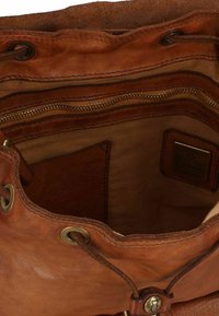 Interno di una borsa a tracolla in pelle marrone con chiusura a cordoncino regolabile, occhielli in metallo e molteplici tasche con zip. Superfici lisce e testurizzate.