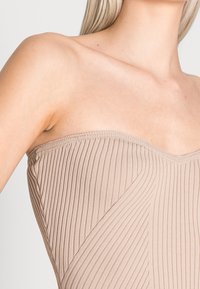 Beige räfflad topp utan axelband med en rak halsringning, som har ett texturerat mönster längs kroppen och en sömlös kant upptill.