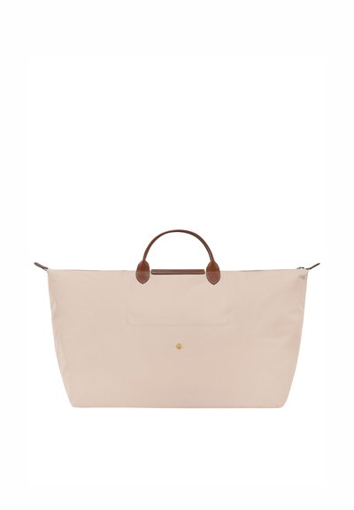 Light pink fabric tote bag with brown leather handles, large zippered opening, and a front pocket. Features a gold logo accent.