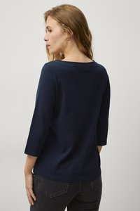 Maglietta a maniche lunghe di colore blu navy con scollo ampio, realizzata in tessuto morbido. Presenta dettagli di cucitura sottili e una vestibilità rilassata attorno alla vita.