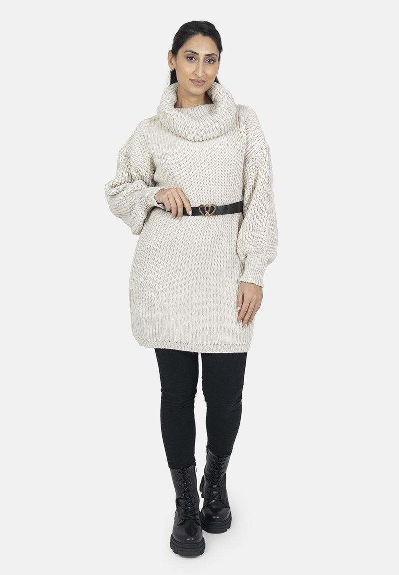 Stickad klänning i krämfärg med en cowl-neck, kombinerad med ett svart bälte med ett hjärtformat spänne, svarta leggings och kängor.