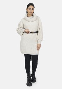 Kremfarvet, ribstrikket sweatdress med stor krave, oversize ærmer og sort bælte med hjerteformet spænde. Bæres med sorte leggings og støvler.