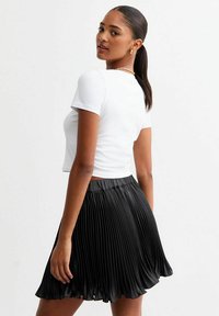 Camiseta blanca corta y falda negra plisada, con tejido suave, textura lisa y cinturilla elástica, que presenta una silueta fluida.