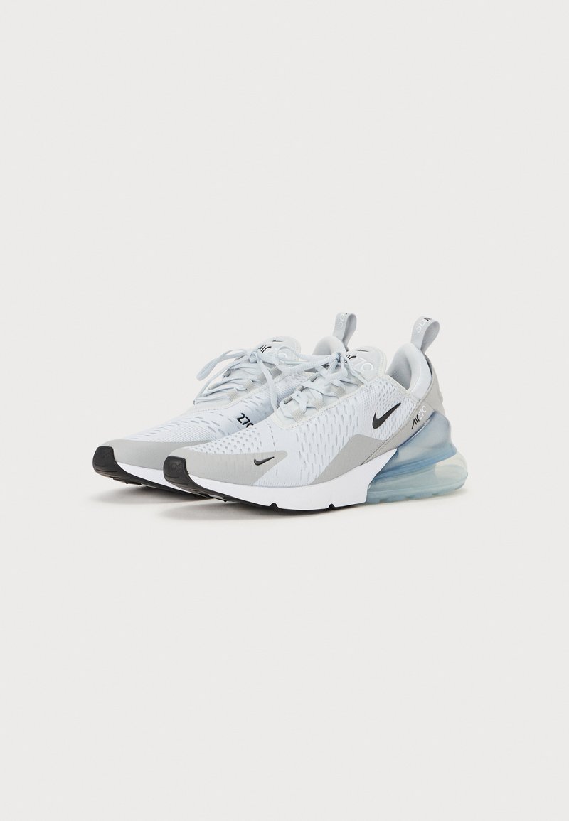 Zapatillas deportivas blancas con material de malla, acentos grises, parte superior texturizada y suela de aire transparente con capuchón de goma negra en la punta y cordones.