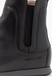 Černá kožená kotníková bota s elastickými bočními vsadkami, hladkou texturou, prošitými detaily a vyraženou značkou na boku.