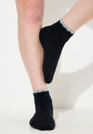 Calze nere a coste con un bordo ondulato azzurro chiaro, realizzate in tessuto a maglia, indossate da un modello su uno sfondo neutro.
