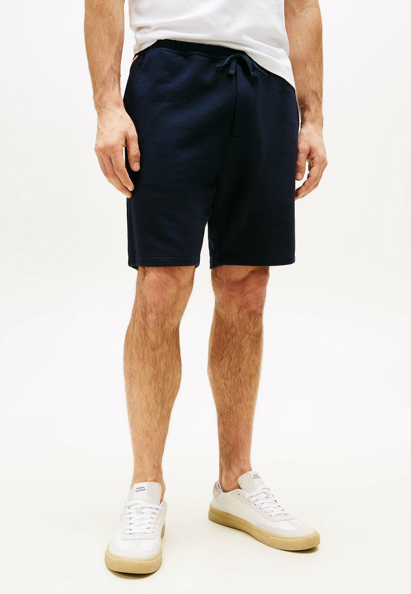 Marineblauwe katoenmengsel shorts met een elastische tailleband en trekkoord, voorzien van zijzakken en een relaxte pasvorm. Gepaard met witte sneakers.
