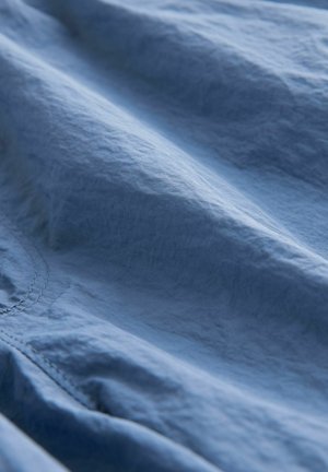 Világoskék szövet, enyhén gyűrött textúrával, amely puha fényt és látható varrási részleteket mutat, jelzi a laza tervezést.