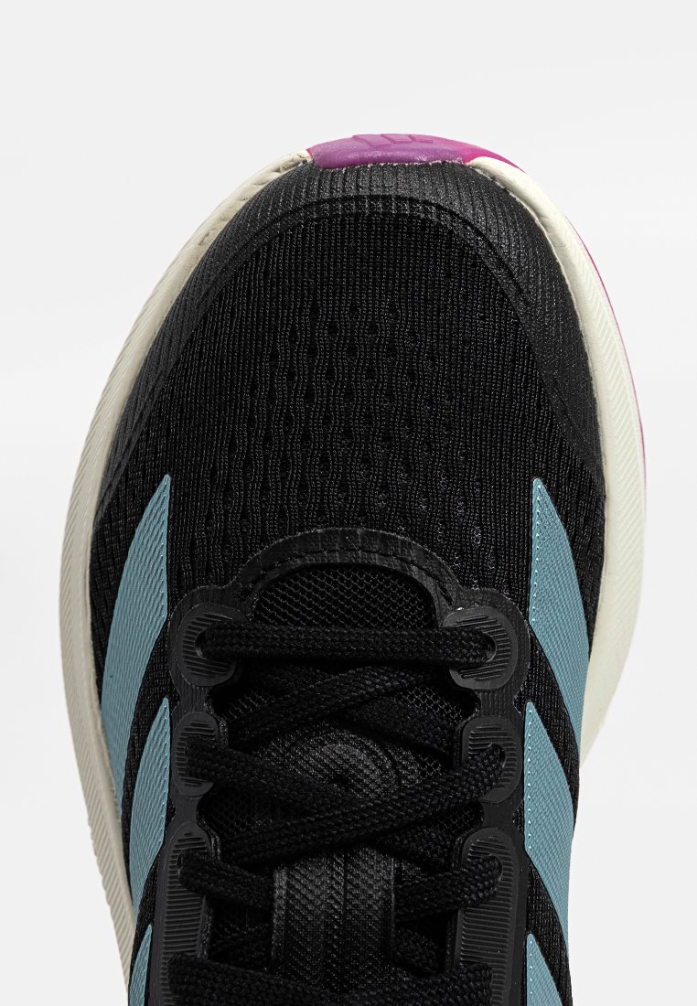 Zapatilla deportiva negra con parte superior de malla texturizada, presenta franjas de acento azul claro, cordones negros y una suela blanca con un detalle de talón morado.
