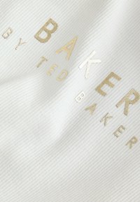 Witte ribstof met gouden folielettering die "BAKER BY TED BAKER" zegt, met variërende hoogtes van de letters.