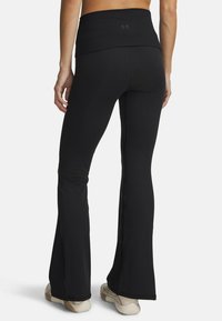 Pantalones de yoga negros acampanados con una cintura ancha, confeccionados con tejido elástico, que presentan una textura suave y un detalle sutil del logo en la parte trasera.