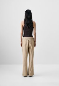 Brun knappet tank topp kombinert med løse, lyse beige teksturerte vide bukser. Buksene har en avslappet midje og milde folde.