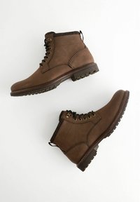 Brown leather ankle boots with a rubber sole, featuring metal eyelets, black laces, and a textured fabric collar.