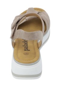 Sandalia de ante beige con diseño de tiras cruzadas, banda elástica y suela de plataforma blanca. Presenta una plantilla acolchada con el logo de la marca en el interior.
