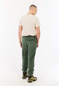 Groen fleece joggingbroek met een textuurafwerking, elastische tailleband en achterzak. Gecombineerd met een beige crewneck t-shirt en wandelschoenen.