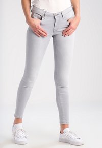 Jeans skinny de mezclilla gris con una cintura de altura media, que cuentan con bolsillos frontales y un ajuste ceñido. Combinados con zapatillas blancas para un look casual.
