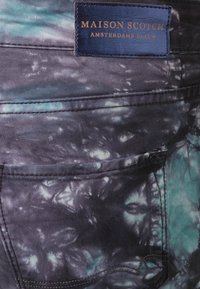Jean en denim avec un motif tie-dye bleu foncé et turquoise, comprenant une poche arrière et une étiquette en cuir indiquant "Maison Scotch Amsterdams Blauw."