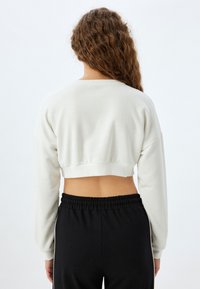 Felpa beige morbida, tagliata, con maniche lunghe e orlo a coste, abbinata a pantaloni neri con coulisse e strisce laterali.