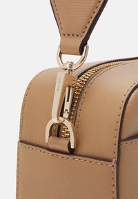 Beige läderhandväska med en guldfärgad dragkedja, med en texturerad yta och metallhardware. Accenterad med kontrasterande brun sömnad.