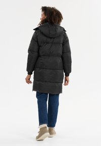 Svart puffjacka med horisontell sömnad, huva och ribbade ärmar; matchad med blå jeans och beige boots. Slät, glansig yta.