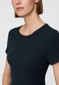 Mørkeblå T-shirt med ribbet struktur, korte ærmer og rund halsudskæring. Stoffet er blødt med en glat tekstur; figursyet silhuet.