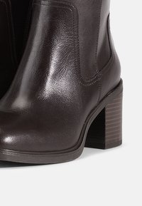 Barna bőr bokacsizma sima felülettel, téglalap alakú sarokkal és oldalsó varrással. Enyhén kerekített orrforma.