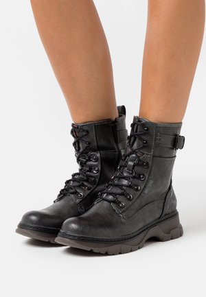 Sorte læderankelstøvler med snørelukning foran, metaløjer og dekorativ spænde i siden. Tekstureret overflade og robust gummiydersål.