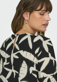 Top de estampado negro y crema con diseños de hojas, espalda con escote en forma de llave y cierre de botón, y una tela texturizada.