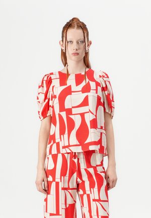 Haut à motifs rouge et crème avec des manches bouffantes et une coupe carrée. Le design présente des formes et des lignes abstraites, créant un impact visuel audacieux.