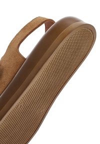 Semelle de sandale en daim marron avec une prise texturée et une bride réglable, montrée de dessous et de côté sur fond blanc.